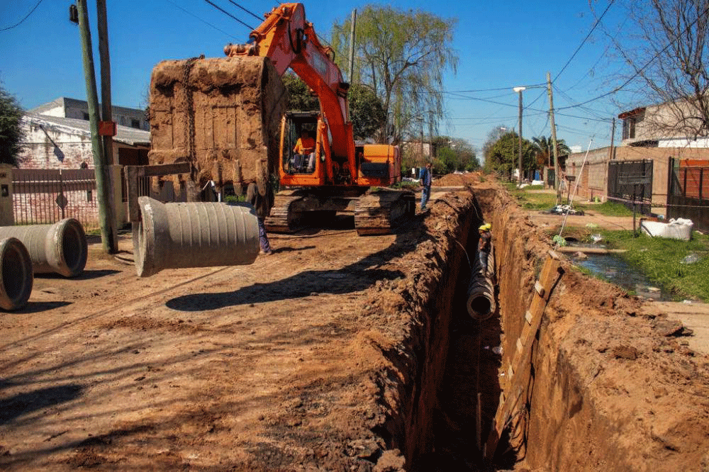 Excavadora colocando caños de hormigón en zanja para tendido cloacal